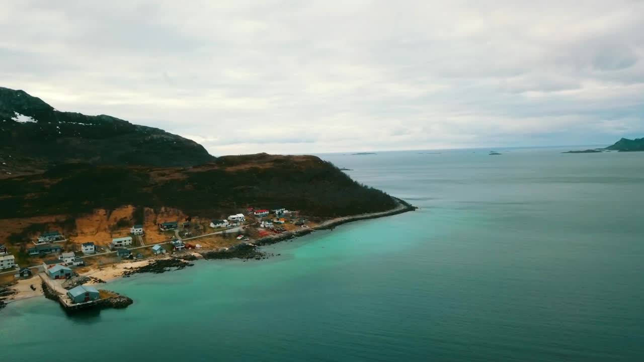 空中拍的房子在雪山的陆地上，无人机在海上向前飞行-特罗姆瑟，挪威视频素材