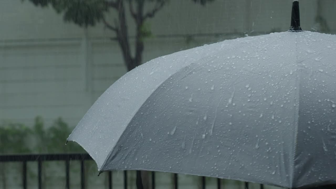 雨落在灰色的伞上。曼谷傍晚雨中的银伞。镜头中的雨滴落在雨伞上。代表恶劣天气冬季或雨季的保护。人和伞在雨中。视频素材