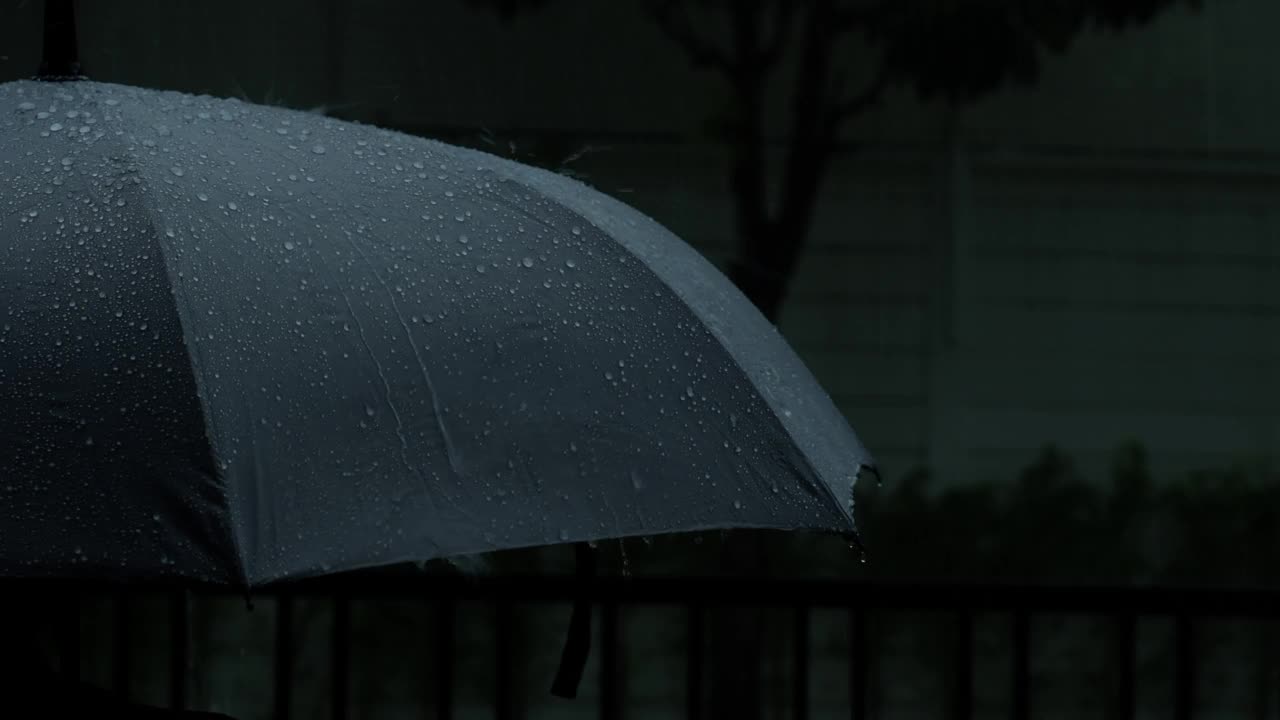 雨落在灰色的伞上。曼谷傍晚雨中的银伞。镜头中的雨滴落在雨伞上。代表恶劣天气冬季或雨季的保护。人和伞在雨中。视频素材