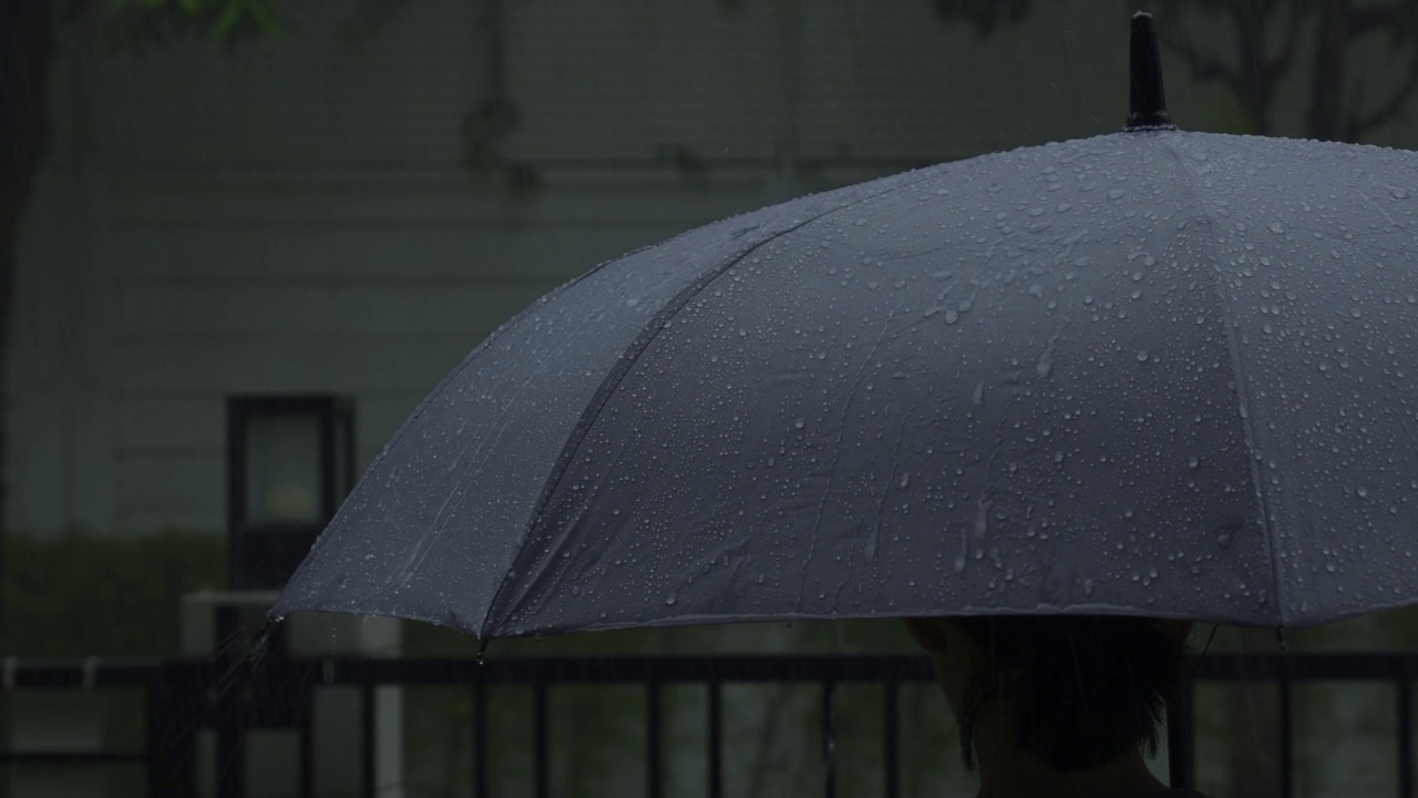 雨落在灰色的伞上。曼谷傍晚雨中的银伞。镜头中的雨滴落在雨伞上。代表恶劣天气冬季或雨季的保护。人和伞在雨中。视频素材