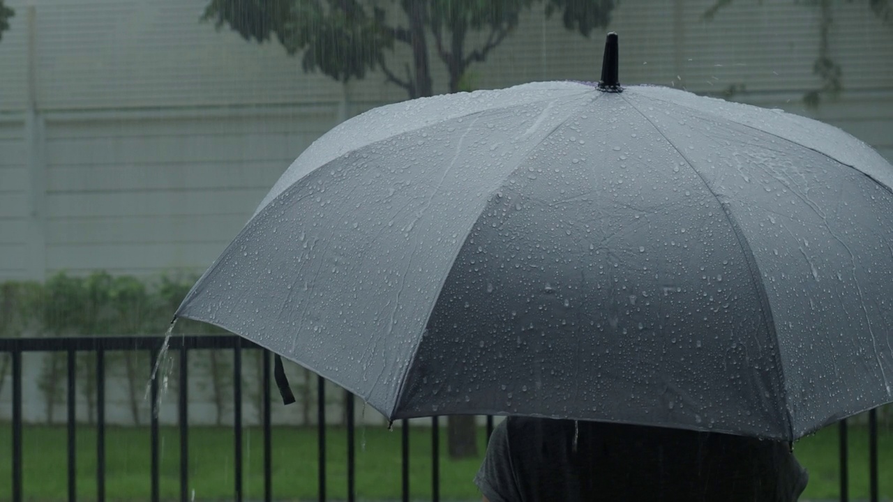 雨落在灰色的伞上。曼谷傍晚雨中的银伞。镜头中的雨滴落在雨伞上。代表恶劣天气冬季或雨季的保护。人和伞在雨中。视频素材