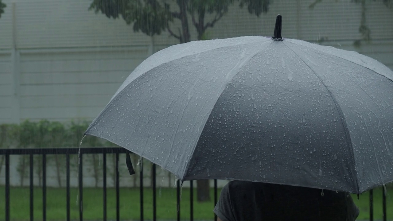 雨落在灰色的伞上。曼谷傍晚雨中的银伞。镜头中的雨滴落在雨伞上。代表恶劣天气冬季或雨季的保护。人和伞在雨中。视频素材