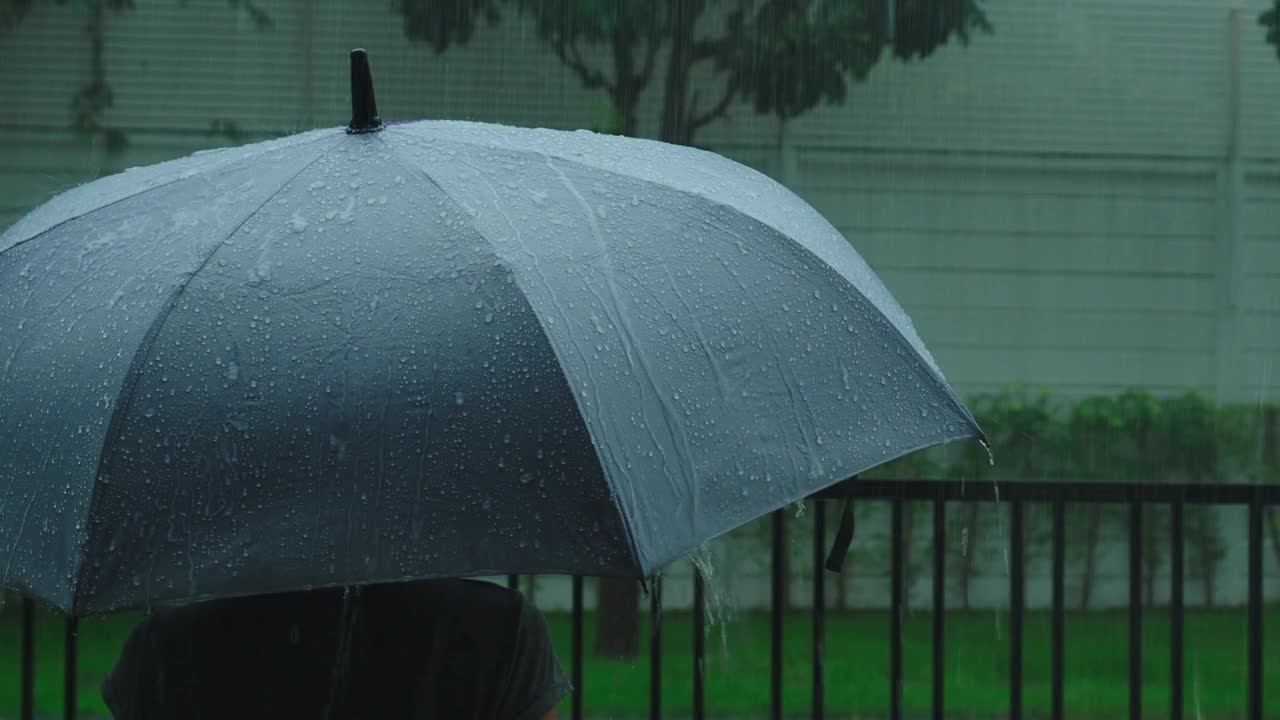 雨落在灰色的伞上。曼谷傍晚雨中的银伞。镜头中的雨滴落在雨伞上。代表恶劣天气冬季或雨季的保护。人和伞在雨中。视频素材