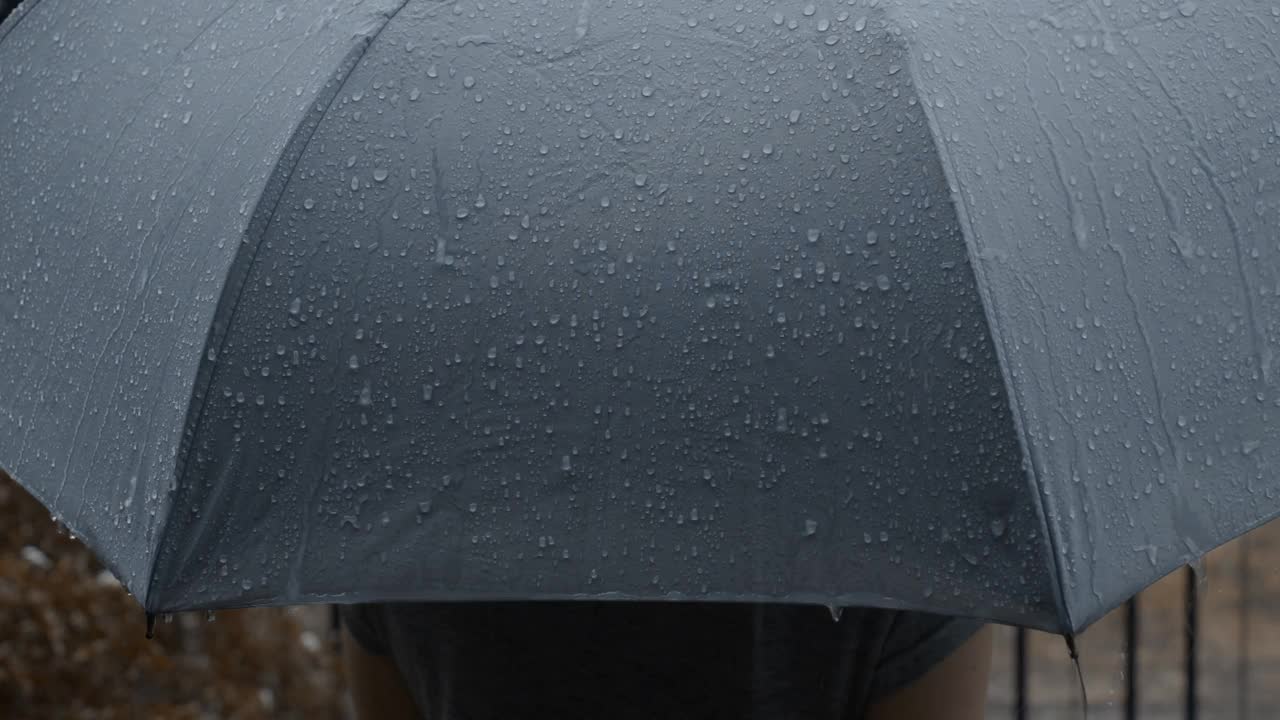 雨落在灰色的伞上。曼谷傍晚雨中的银伞。镜头中的雨滴落在雨伞上。代表恶劣天气冬季或雨季的保护。人和伞在雨中。视频素材