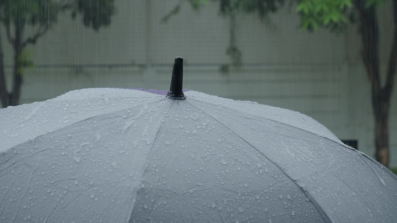 雨落在灰色的伞上。曼谷傍晚雨中的银伞。镜头中的雨滴落在雨伞上。代表恶劣天气冬季或雨季的保护。人和伞在雨中。视频素材