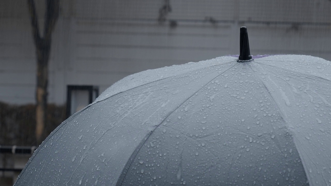 雨落在灰色的伞上。曼谷傍晚雨中的银伞。镜头中的雨滴落在雨伞上。代表恶劣天气冬季或雨季的保护。人和伞在雨中。视频素材