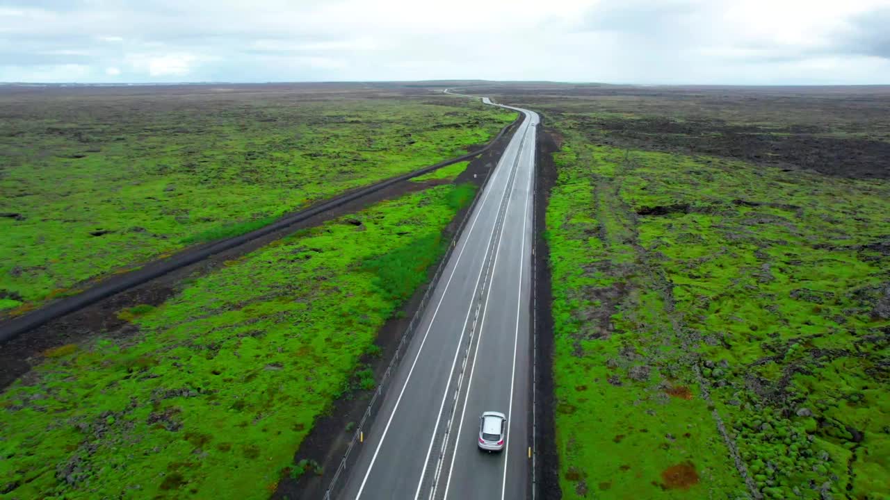 航拍镜头跟踪汽车在笔直的道路上与冰岛的熔岩平原景观。视频素材