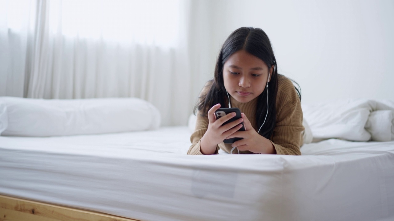 亚洲女孩躺在床上喜欢用手机听音乐白天在家里视频素材