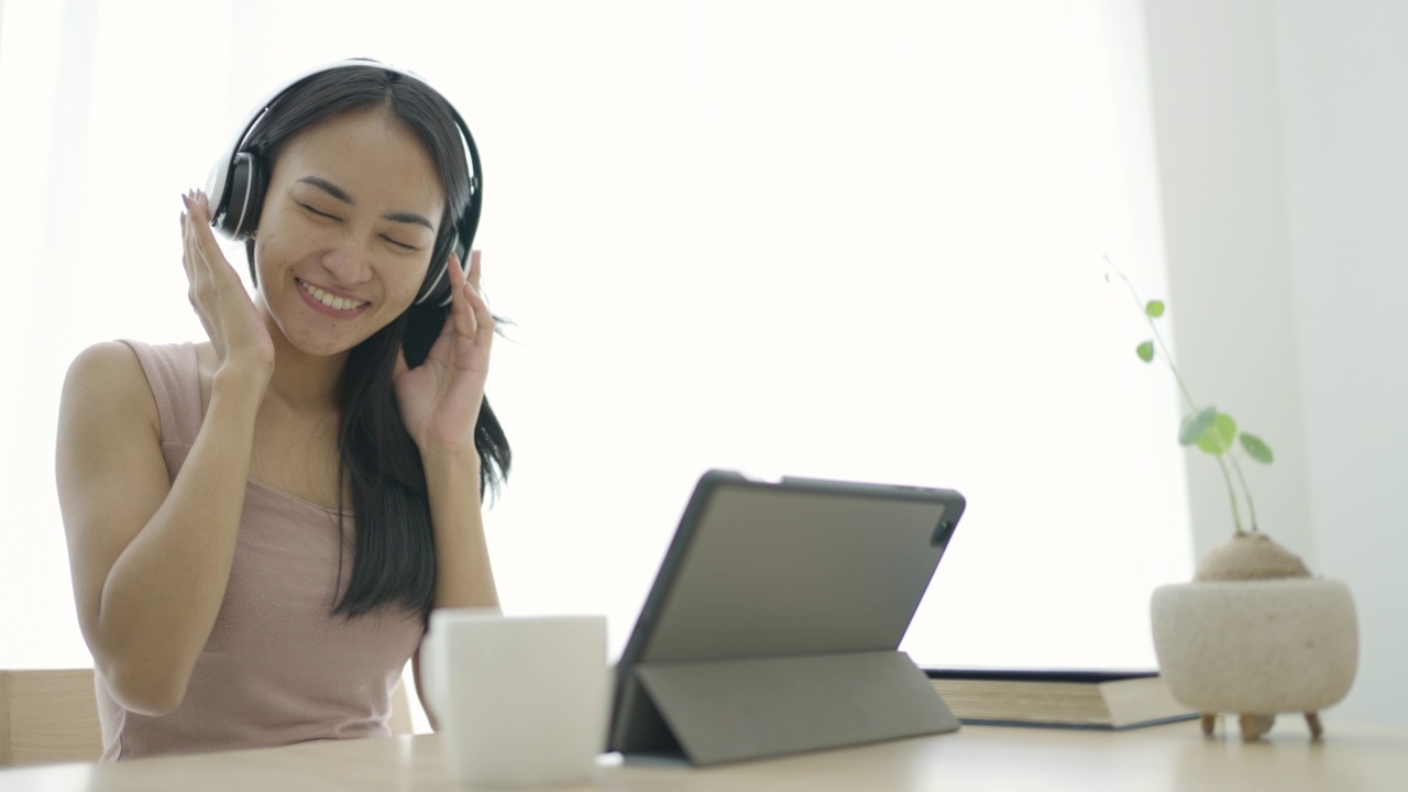 年轻的亚洲女子放松在沙发和听音乐与耳机在客厅在家里视频素材