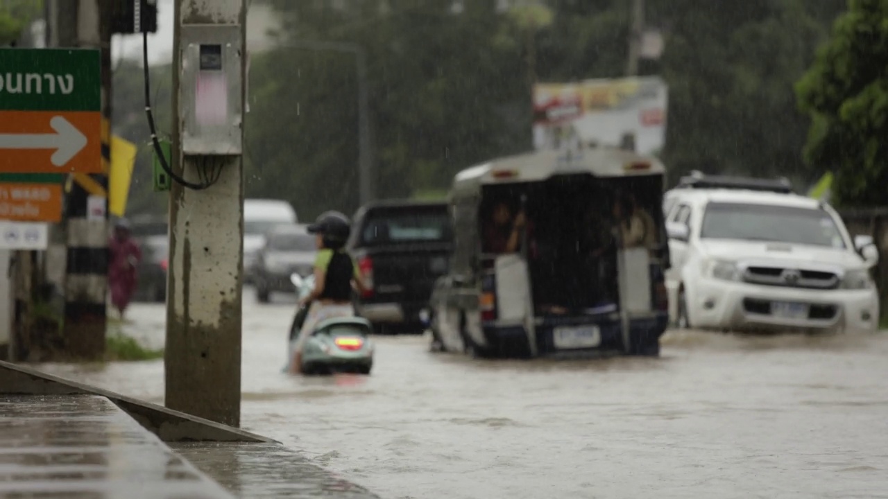 在暴雨引发的洪水中行驶在被淹道路上的汽车。雨下着，汽车跑在满是水的路上。视频素材