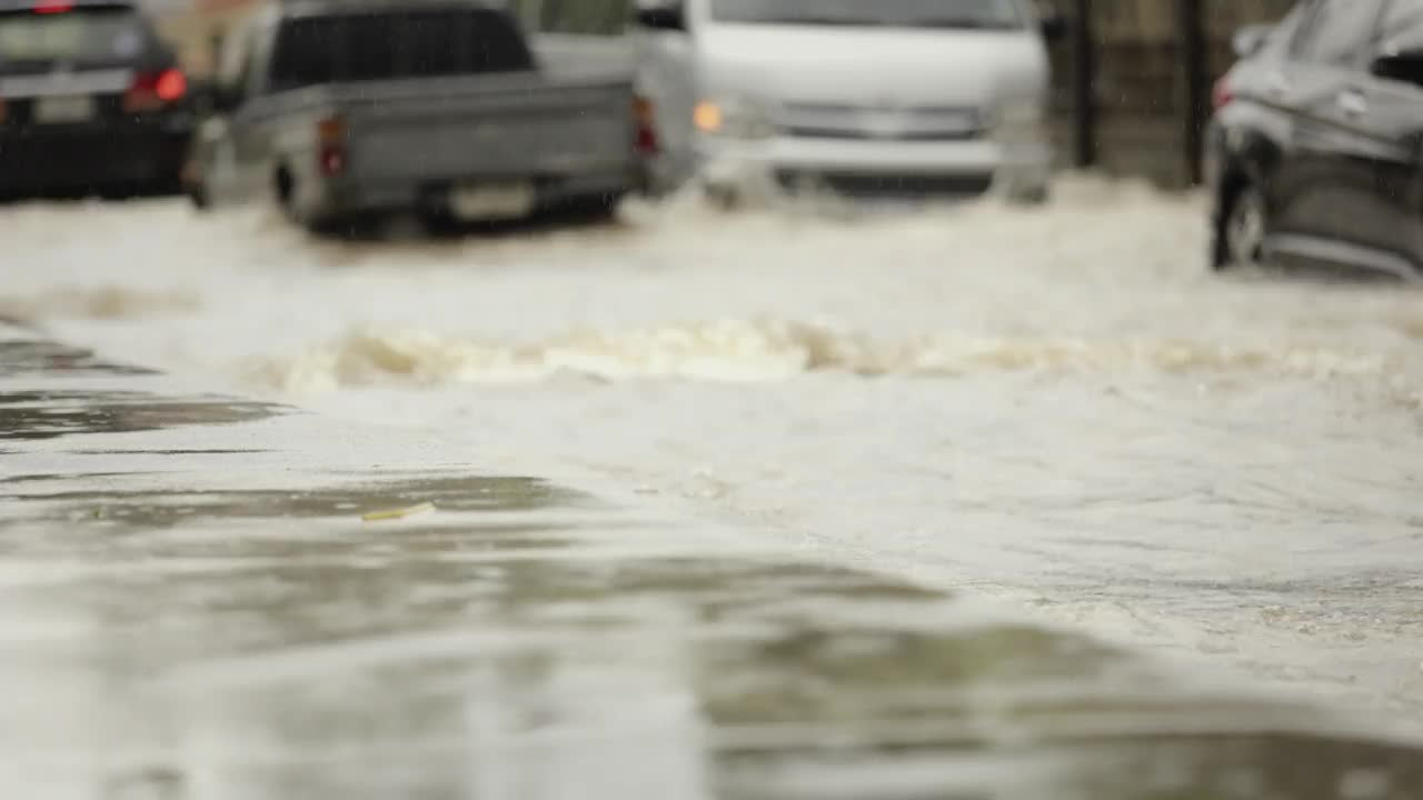 在暴雨引发的洪水中行驶在被淹道路上的汽车。雨下着，汽车跑在满是水的路上。视频素材