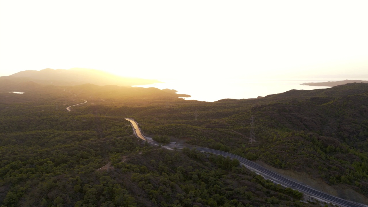 山林之间的柏油路，后面的大海和壮丽的日落，无人机的视野视频素材