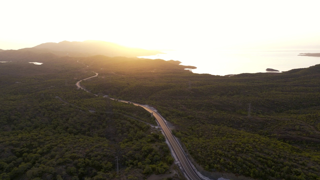 山林之间的柏油路，后面的大海和壮丽的日落，无人机的视野视频素材