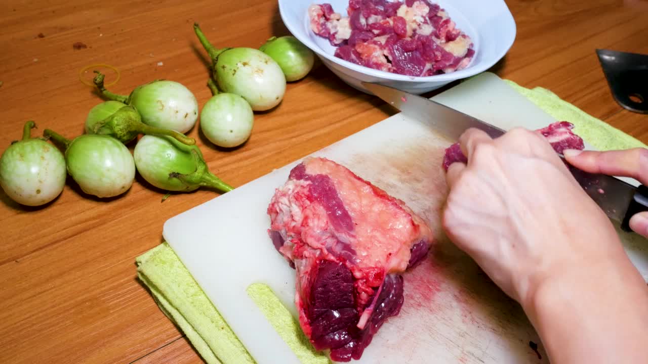 女人的手用菜刀切生牛肉。在家里的厨房里煮肉菜，在家里的厨房里切鲜肉。的一面。视频素材