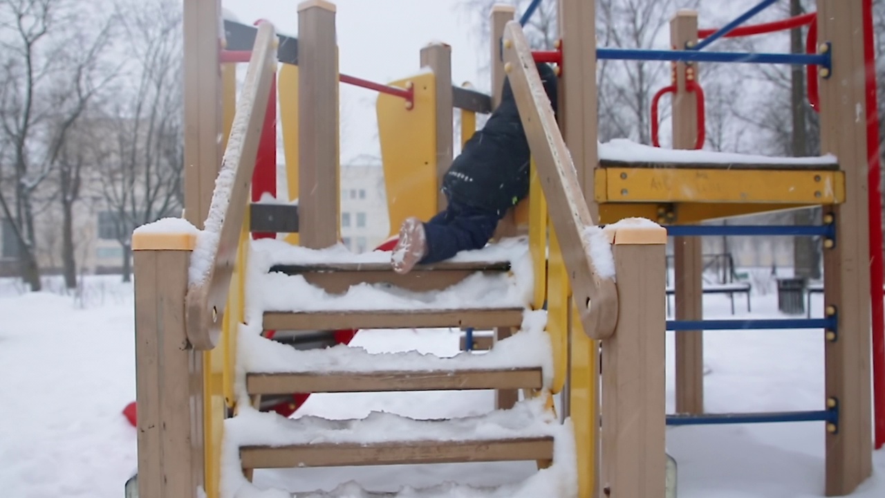 一个小男孩在雪地台阶上爬儿童滑梯。视频下载