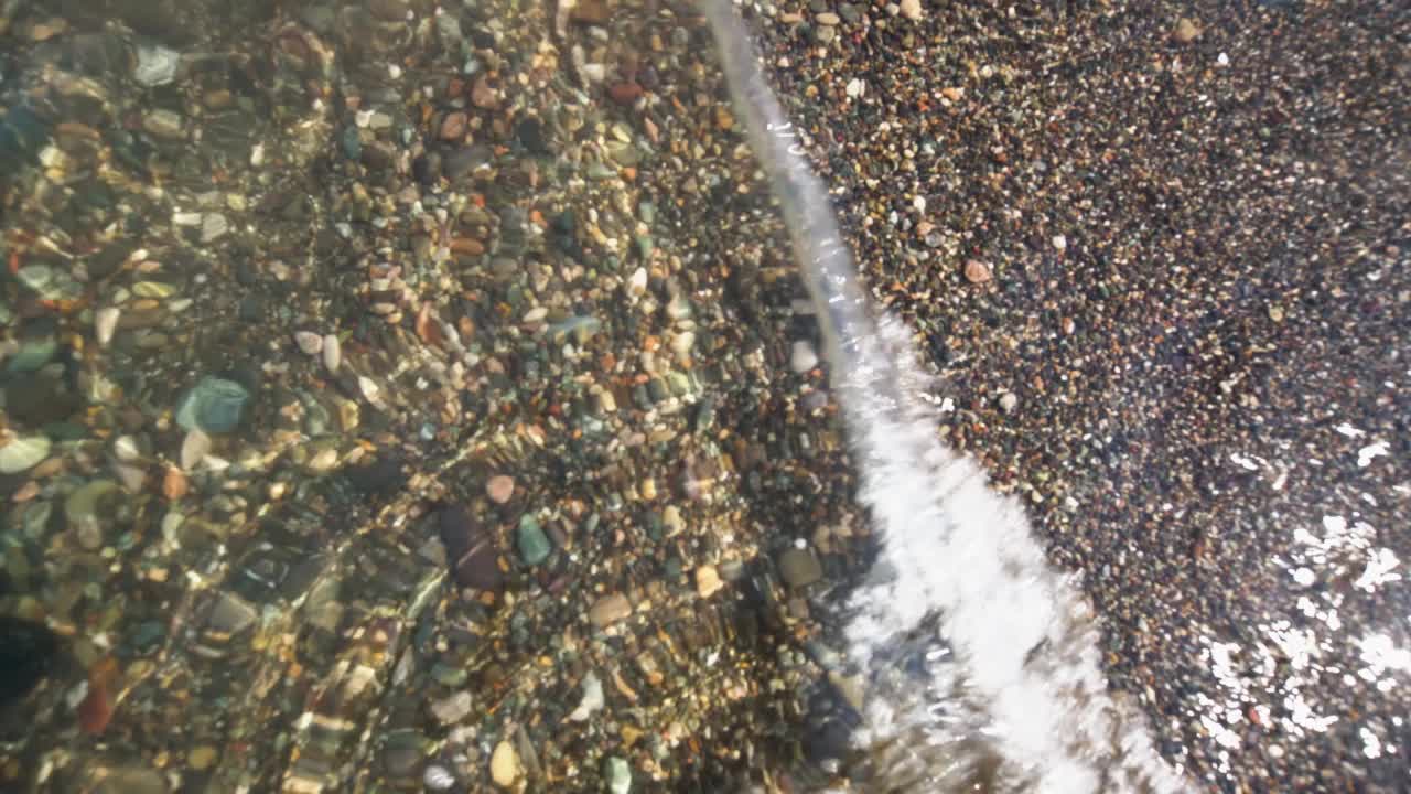 卵石滩在清澈的海水和波浪下。海滩上水下的鹅卵石特写。视频素材