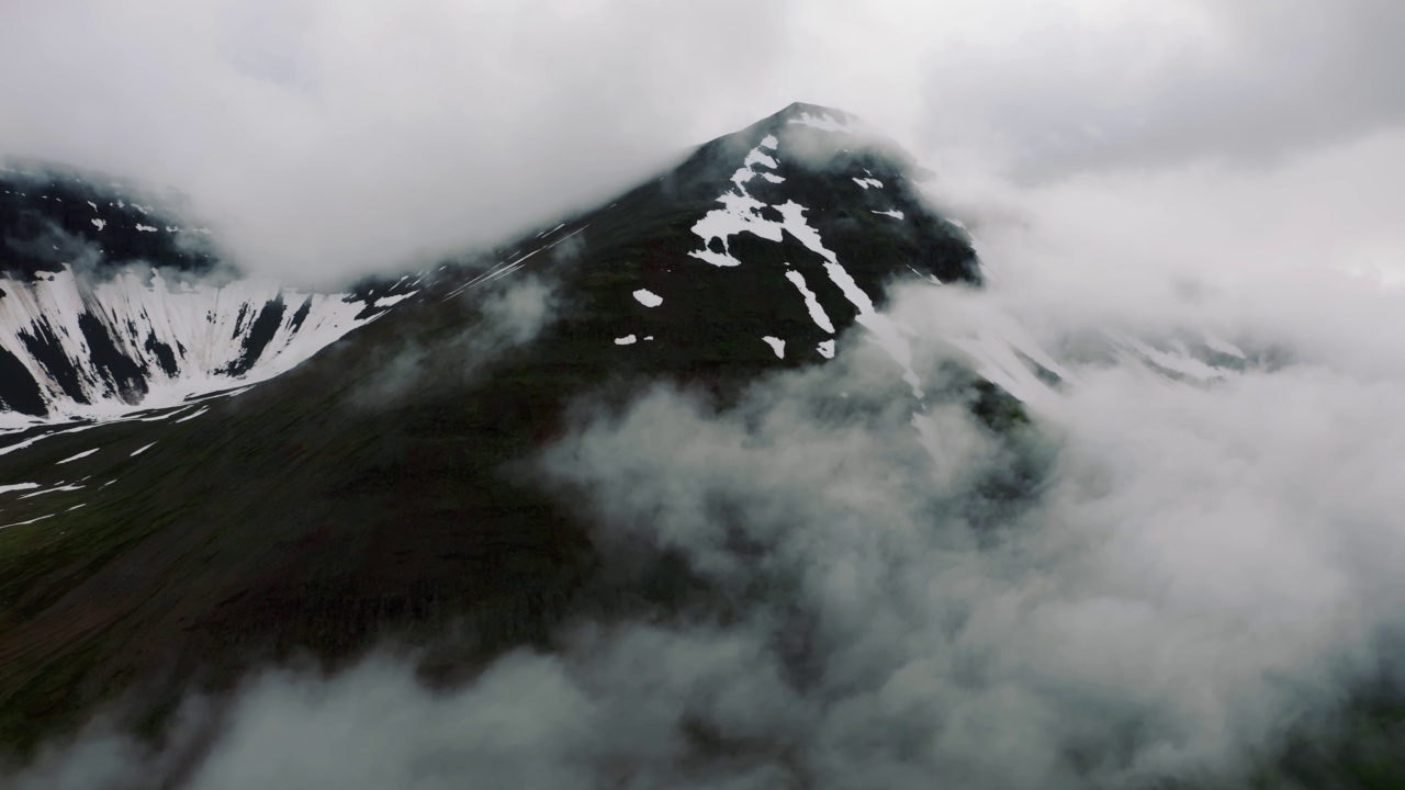 鸟瞰北欧风景，飞越美丽的雪山覆盖着滚动的雨云，美丽的形成在冰岛。电影无人机拍摄的惊人的北部悬崖视频素材