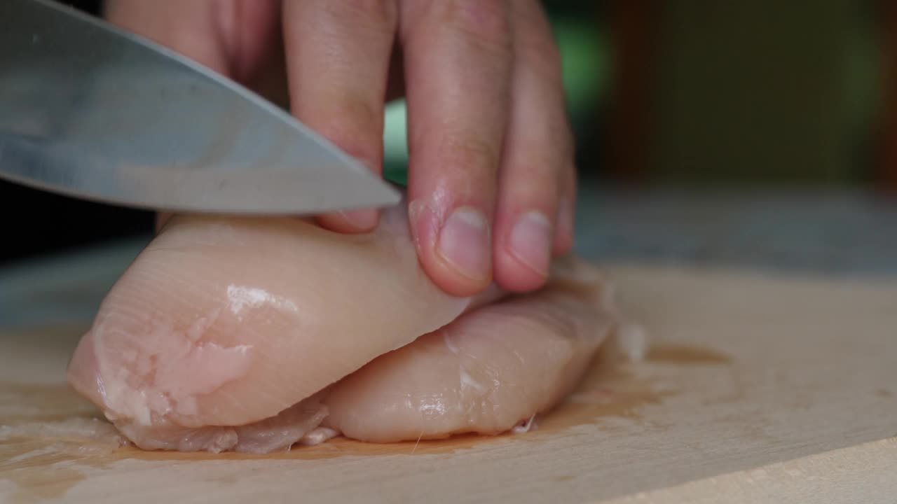 切板上的鸡肉片。男子用刀将精致的火鸡片切在砧板上。厨师切鸡胸肉，生白肉，厨师煮鸡胸肉，饮食健康饮食。视频素材