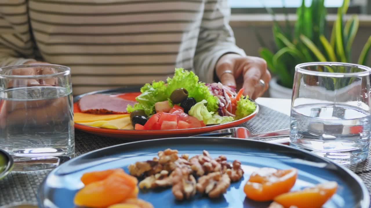 年轻女子在酒店的咖啡馆里吃着漂亮美味的早餐。蔬菜沙拉，橄榄，香肠，培根，西红柿，青豆。自助餐，欧式早餐慢镜头视频素材