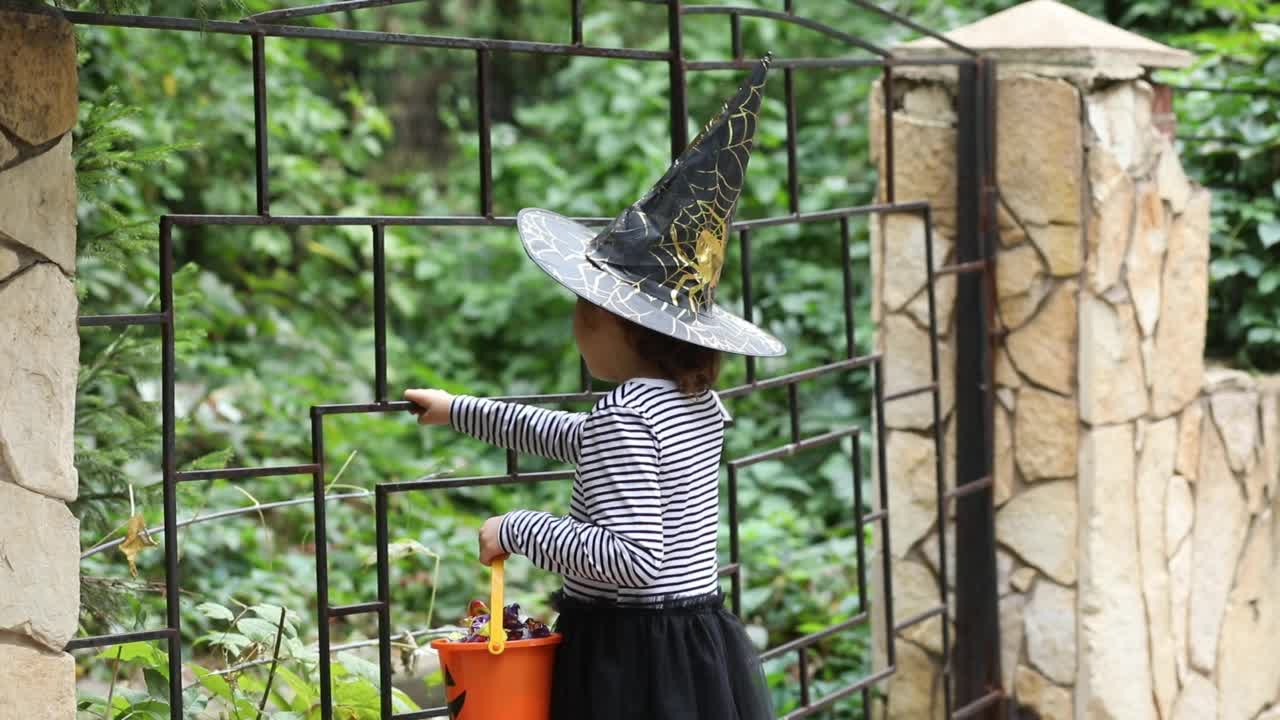 小可爱的女孩在女巫服装拿着南瓜灯桶糖果和招待糖果。孩子们在万圣节玩得很开心。视频素材