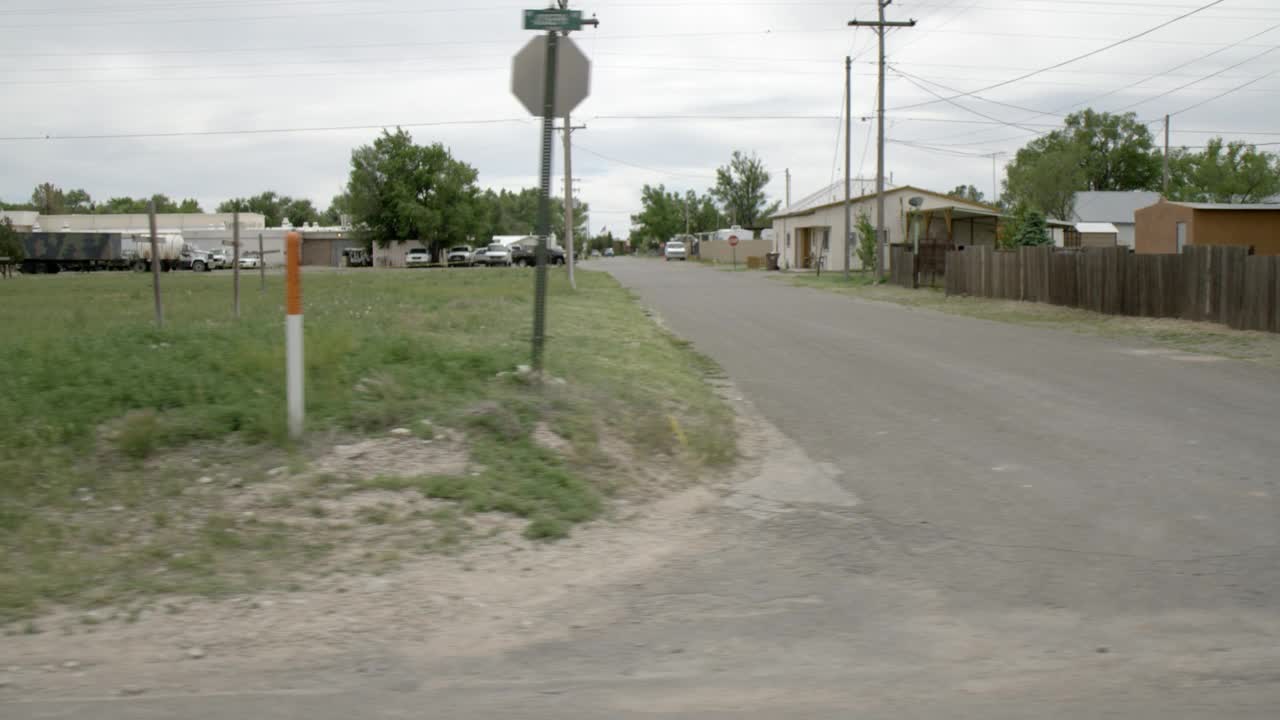 慢行或慢行过程中，沿乡村道路直的乡村右侧。一层的房子，十字架，树木和废墟可以在田野中看到。阴视频素材