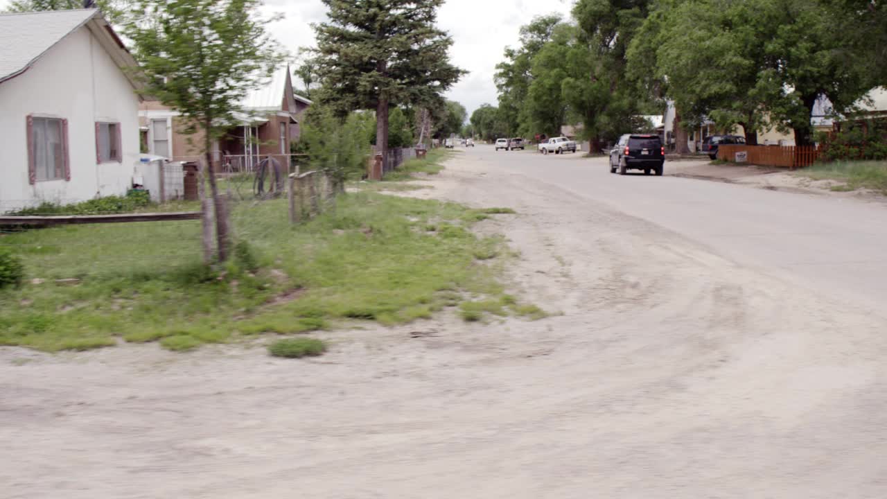 慢行或慢行过程中，沿乡村道路直的乡村右侧。一层楼的房子、破旧的栅栏、大门、树木和瓦砾在院子和田野里随处可见。人们在门廊上闲逛。阴视频素材