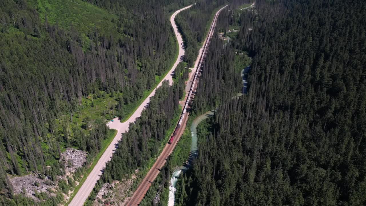 鸟瞰郁郁葱葱的山谷与火车在铁路，河流，森林和高速公路视频素材