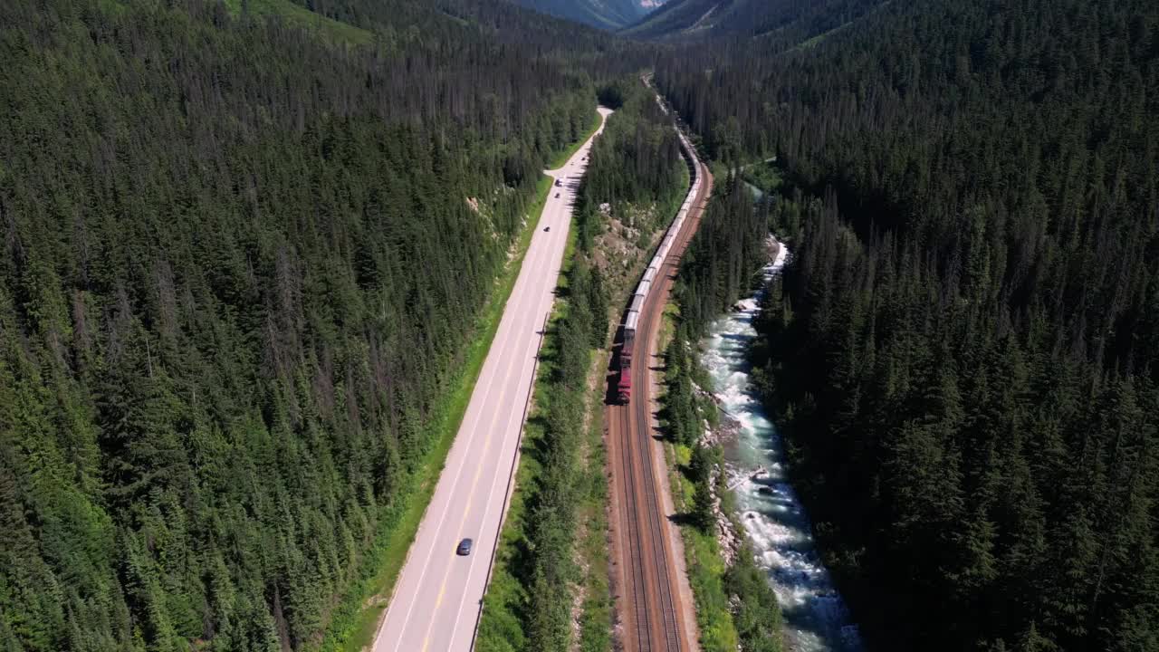 鸟瞰郁郁葱葱的山谷与火车在铁路，河流，森林和高速公路视频素材