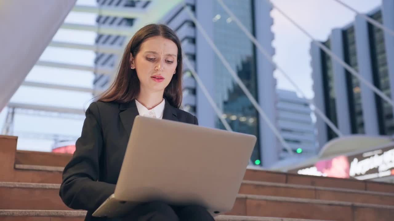 白种人年轻的商人和妇女，晚上在城市的户外工作。有吸引力的男女员工使用笔记本电脑进行网上交流聊天，完成紧急工作。视频素材