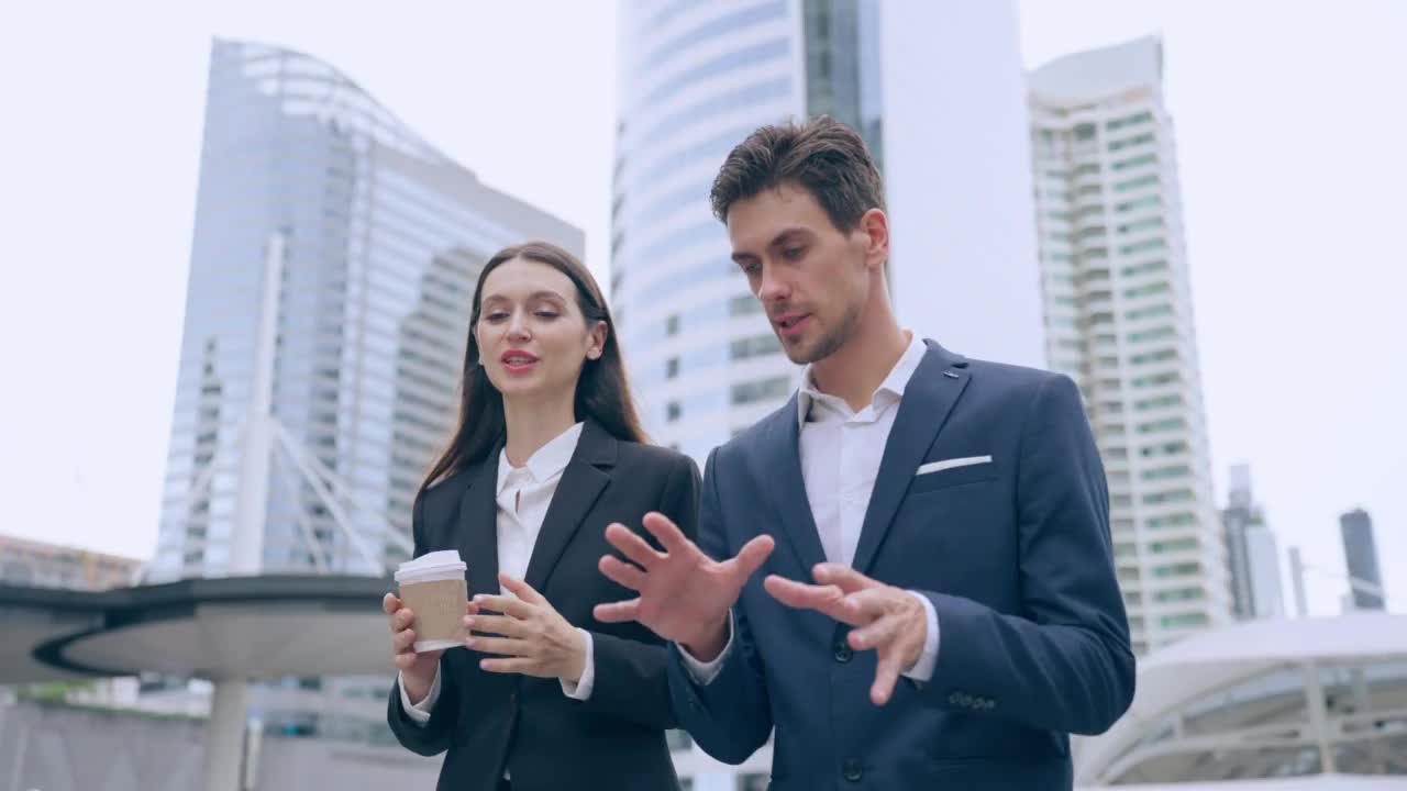 白人商人和女商人走在城市的户外。有魅力的年轻男女员工一边谈论着，一边计划着一个项目，一边走到办公室外面。视频素材