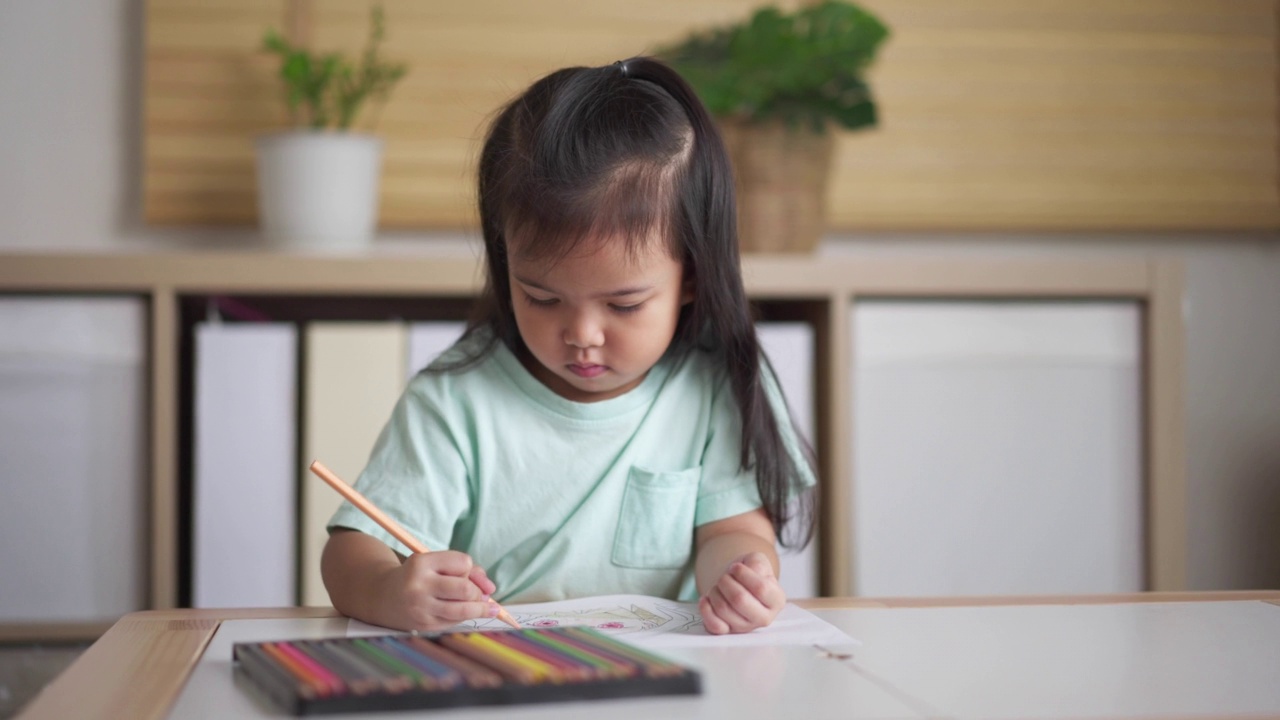 小女孩喜欢在家里客厅的纸上用彩色铅笔涂色或绘画。儿童技能发展与艺术教育视频素材