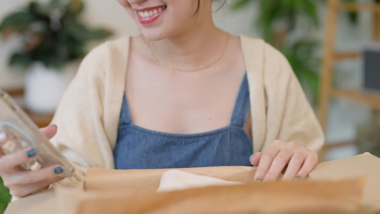 年轻的亚洲妇女从纸箱中打开新购买的衣服，从她的网上购物零售送货上门。视频素材