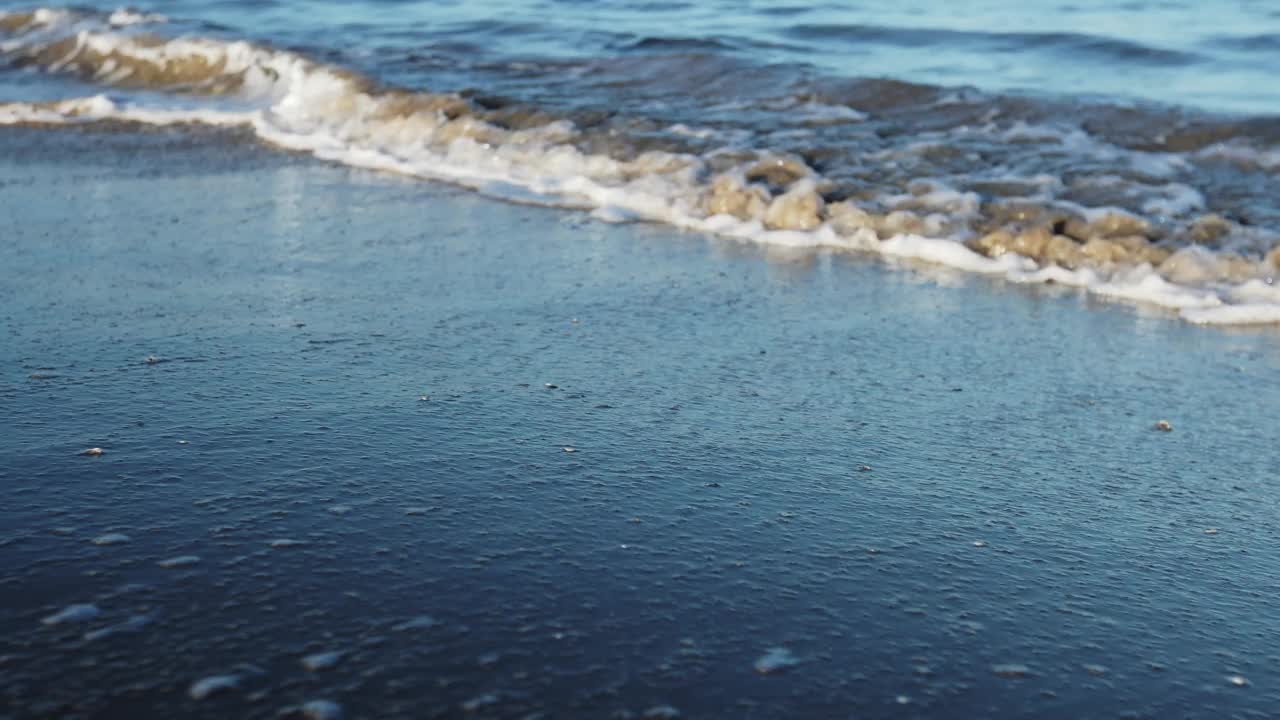 夕阳下的沙滩上，海浪拍打着海岸。蓝绿色波浪的飞溅视频素材