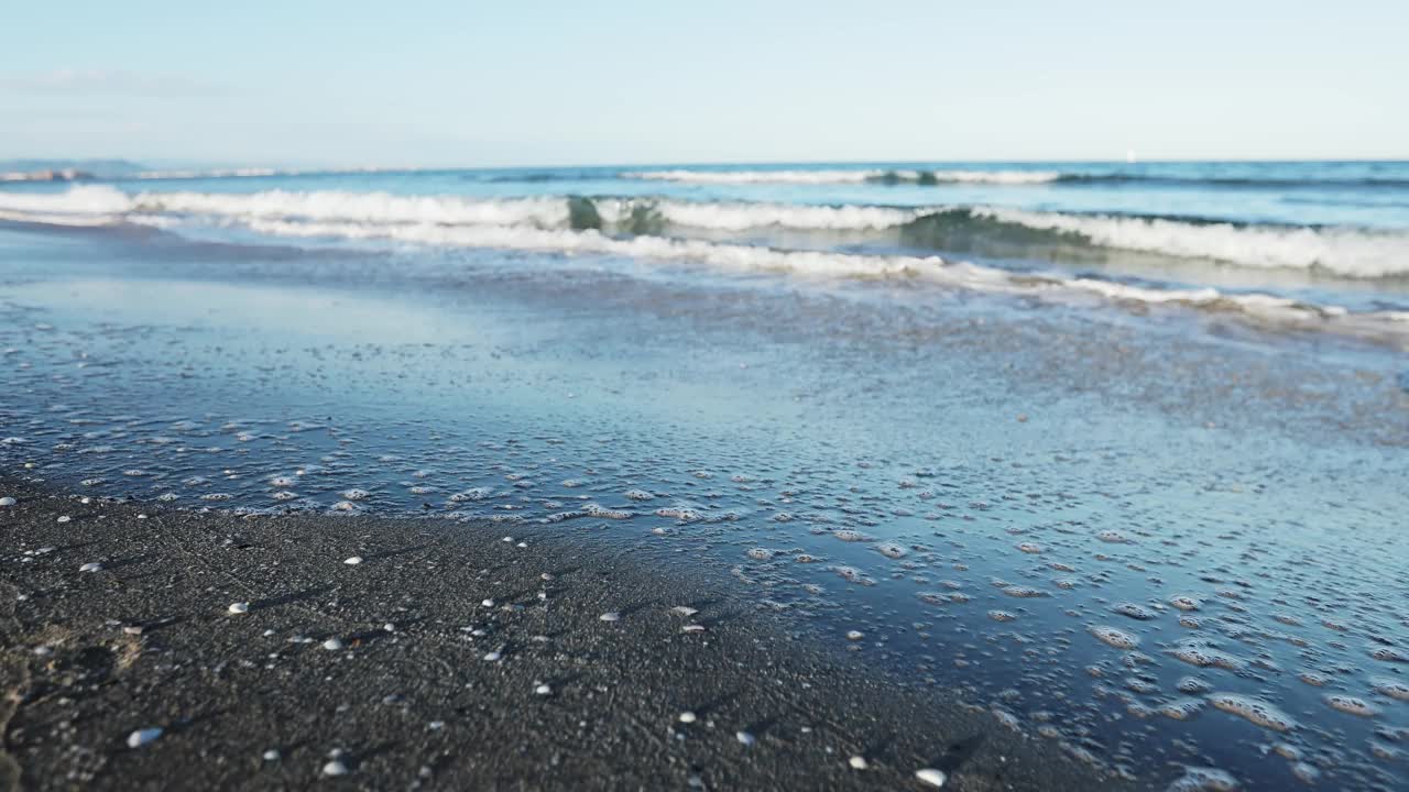 夕阳下的沙滩上，海浪拍打着海岸。蓝绿色波浪的飞溅视频素材