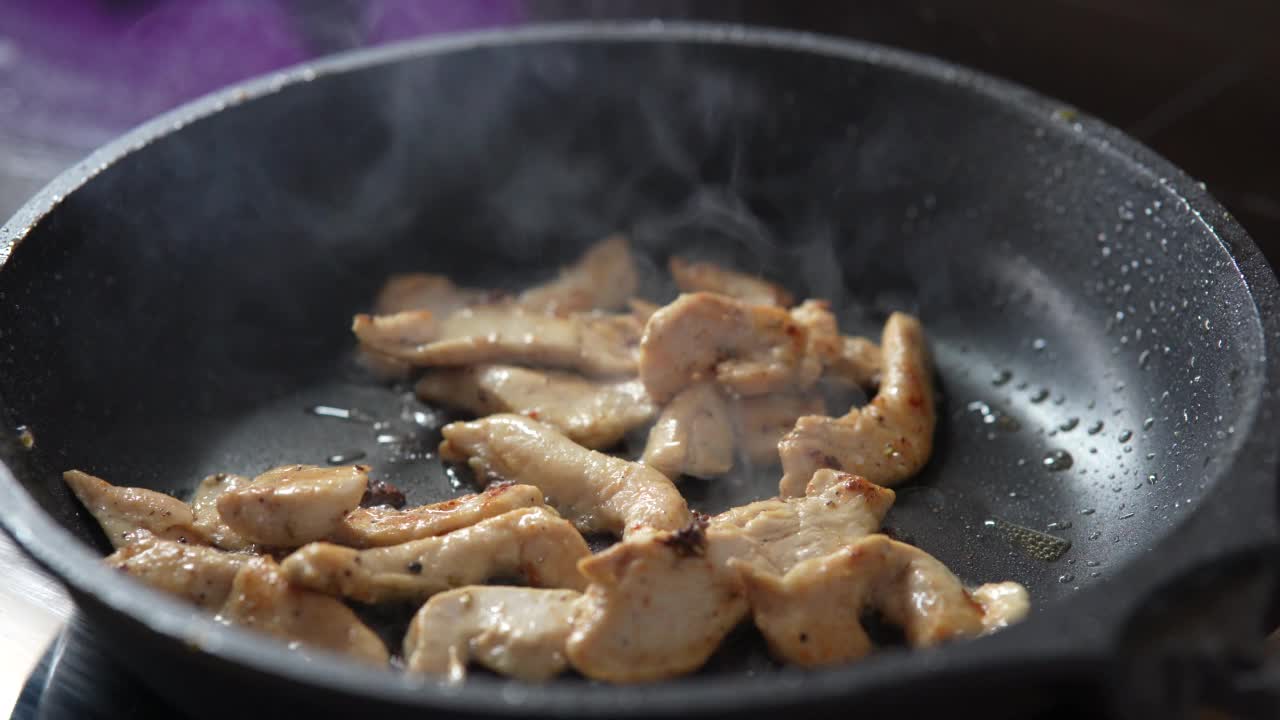 把肉块放在煎锅里煎。在煎锅中用热油煎鸡肉，特写。视频素材