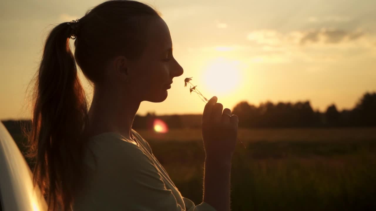 夕阳下微笑的年轻女子享受着一束雏菊的花香视频素材