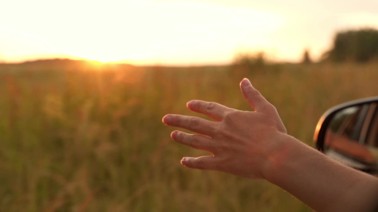 在夕阳的背景下，一个快乐的女人从车窗伸出手来。女司机开车时把手伸出车窗外视频素材