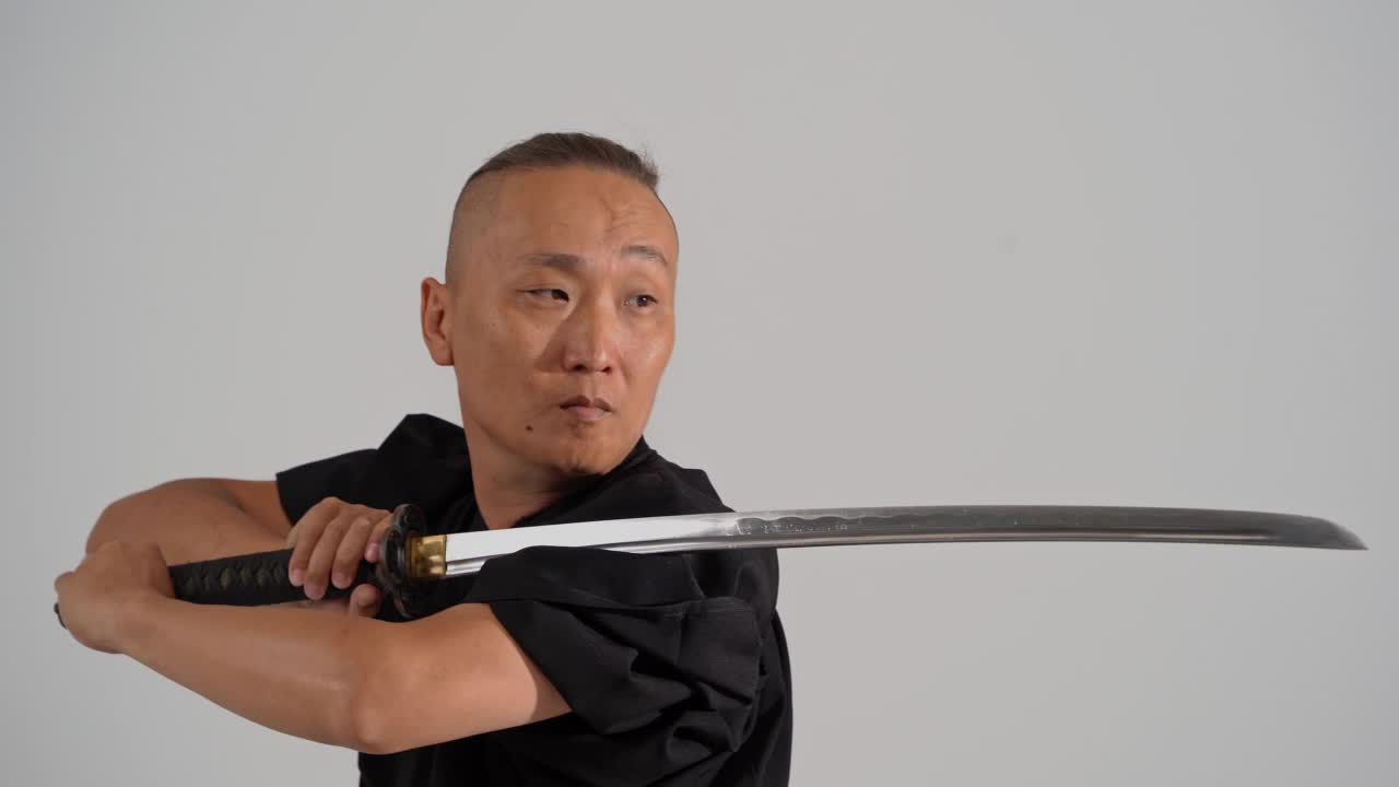 日本武士穿着黑色和服，手里拿着武士刀，在白色的画室里视频下载