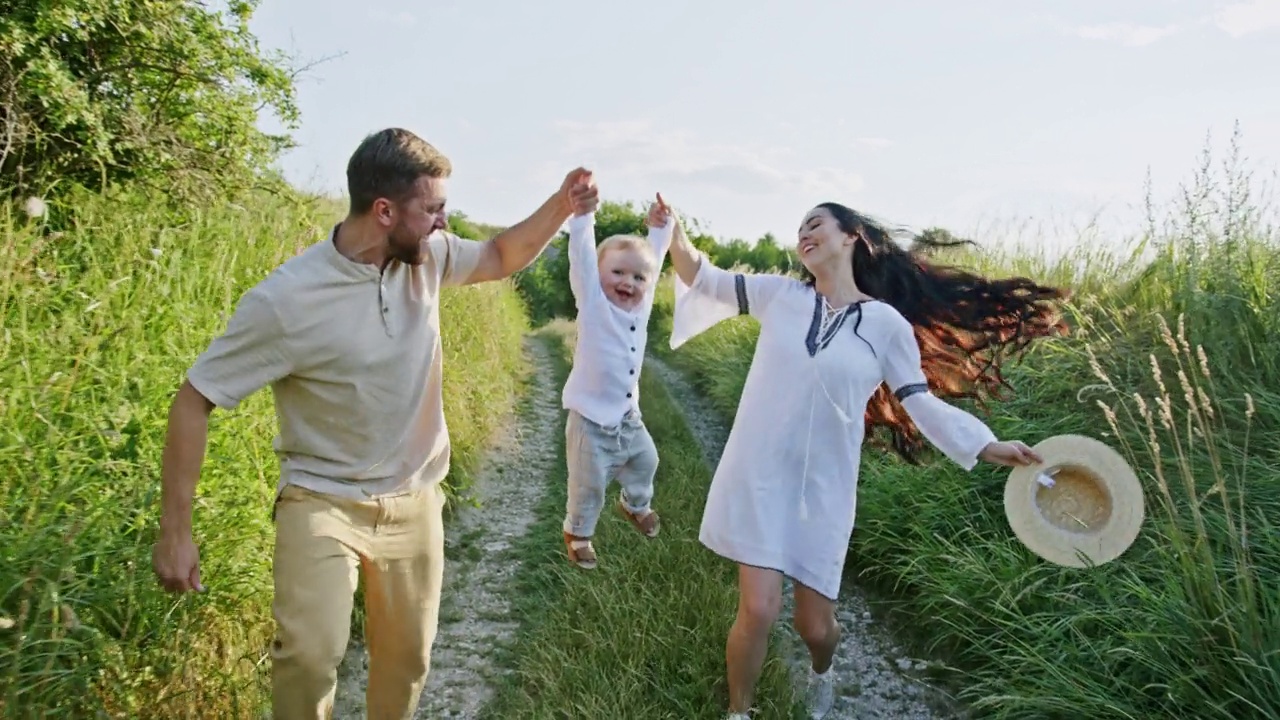 快乐快乐的年轻父母带着他们的婴儿在乡间小路上奔跑，把婴儿举在空中视频素材
