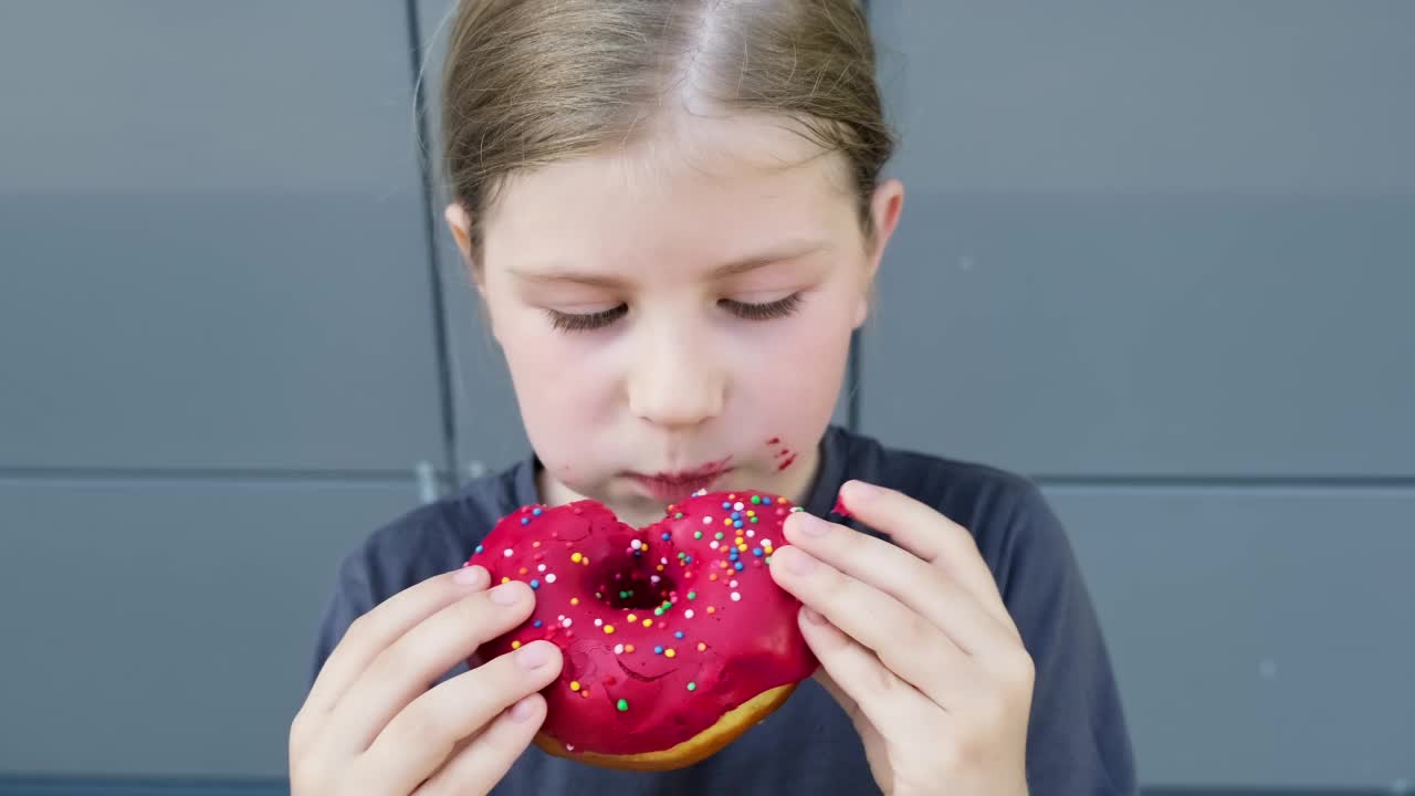 孩子在享受甜甜圈甜点。吃粉色甜甜圈的女孩。不健康食品的概念。视频素材