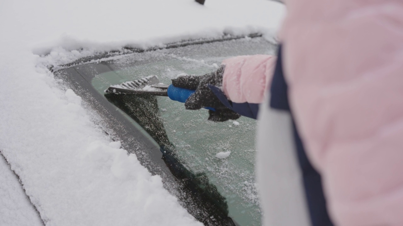 女人正在用刮刀清理他车上的积雪，慢动作视频素材