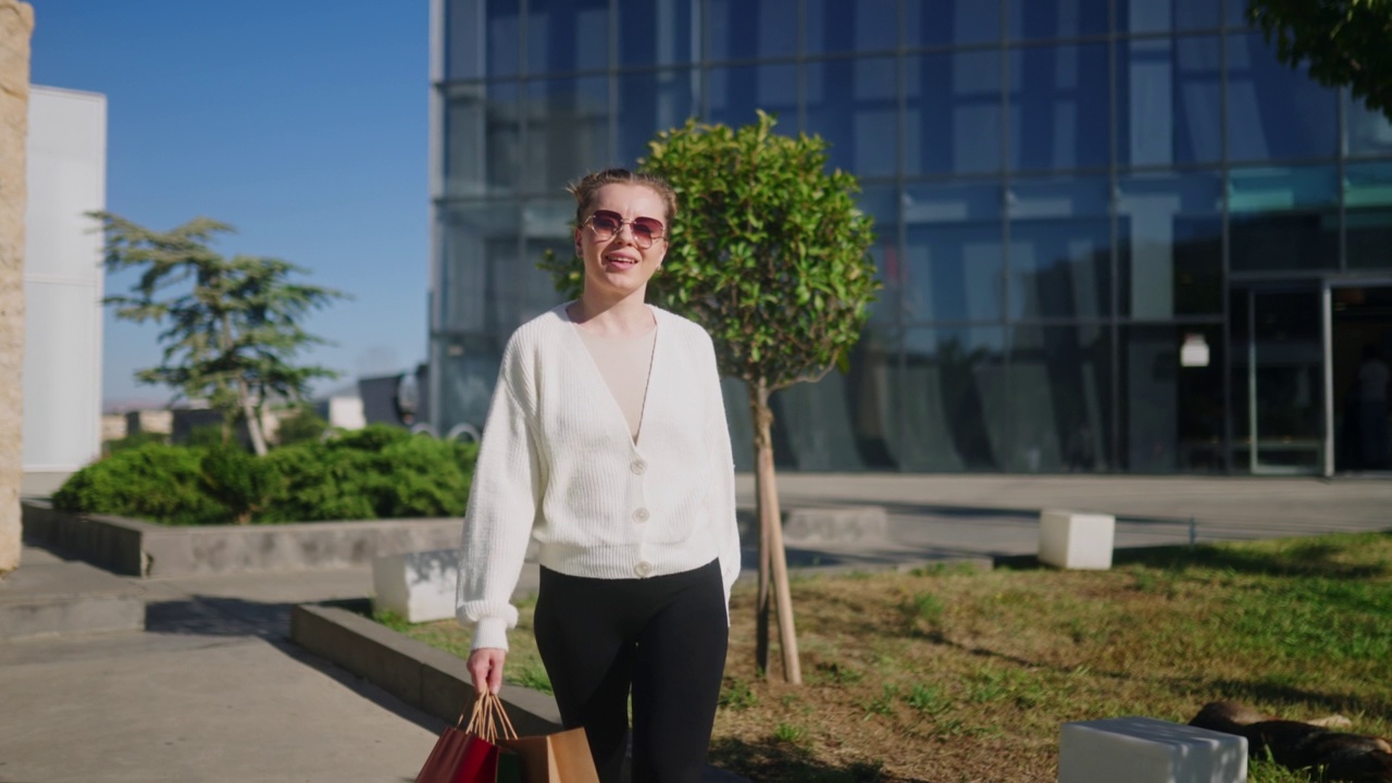 快乐的女人带着购物袋从商场走在城市里。兴奋的女孩享受黑色星期五大减价。女人们拿着满满的纸袋在镜头前跳舞摆姿势。消费主义的概念。缓慢的运动。视频素材