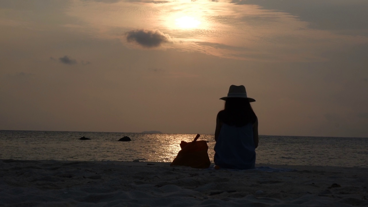 快乐的女人坐在夕阳下的海滩上视频素材