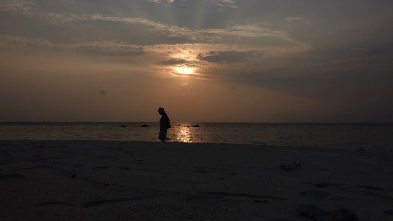 夕阳西下，走在海滩上的女人视频素材