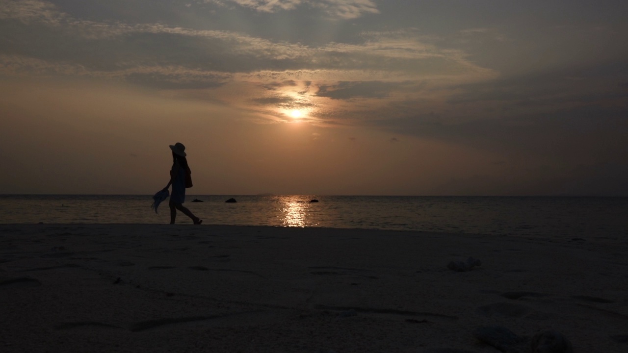 夕阳西下，走在海滩上的女人视频素材