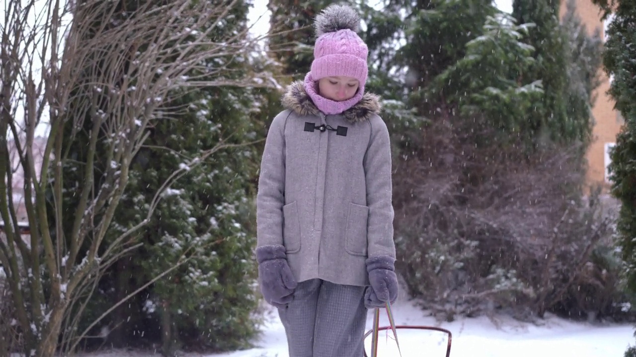 悲伤的少女拉着雪橇慢动作走在后院离开。肖像不安的白人青少年在户外散步，白雪飘落在冬天的一天。青春期与悲伤的概念。视频素材