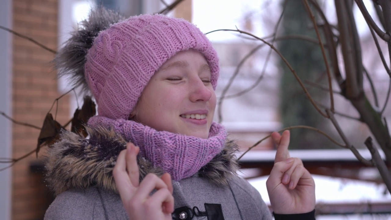 特写积极的十几岁女孩交叉手指在慢动作许愿站在户外在下雪的冬天的一天。自信的白人少年希望奇迹欣赏雪花。视频素材