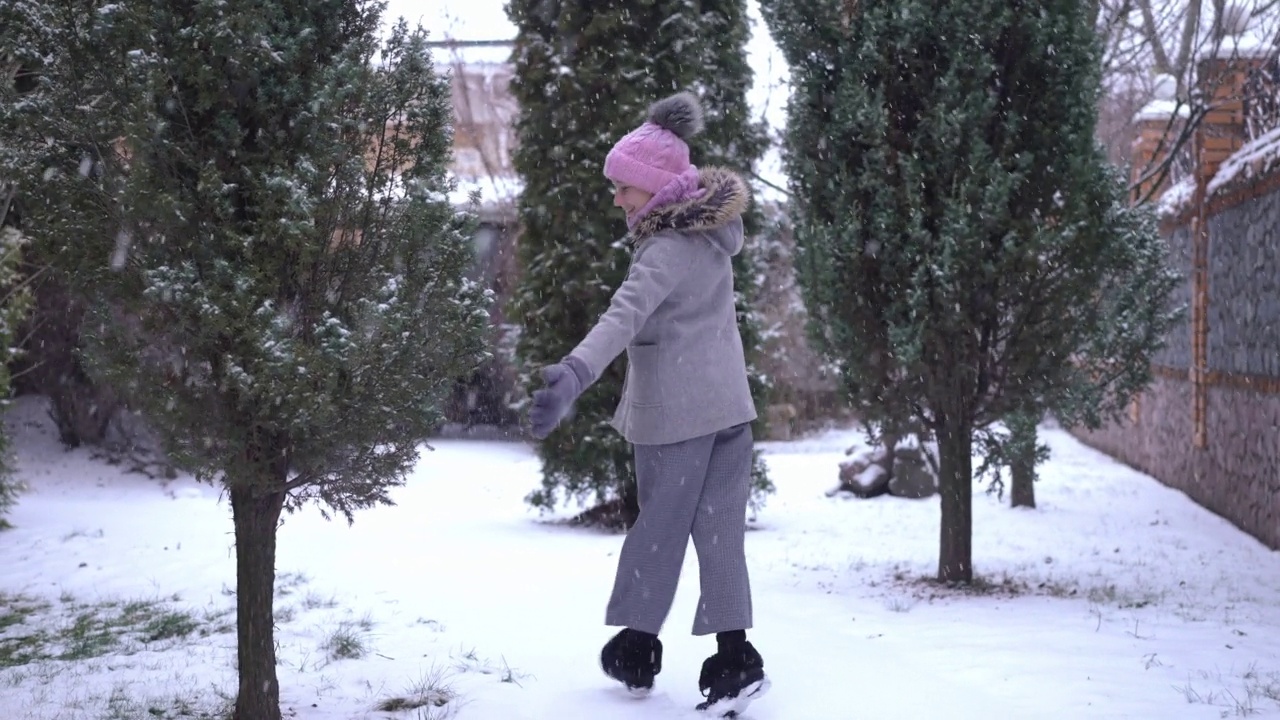 跟踪拍摄快乐的少女看着相机旋转在雪天冬天走在后院。快乐兴奋的白人少年欣喜白色的雪在慢动作户外。视频素材