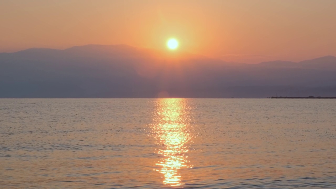 平静海面上令人惊叹的美丽日出。黄色的太阳从海上和山上升起，太阳的路径在水上。阳光和太阳光反射在水面上。金色的光，橙色和金色的蓝天视频素材