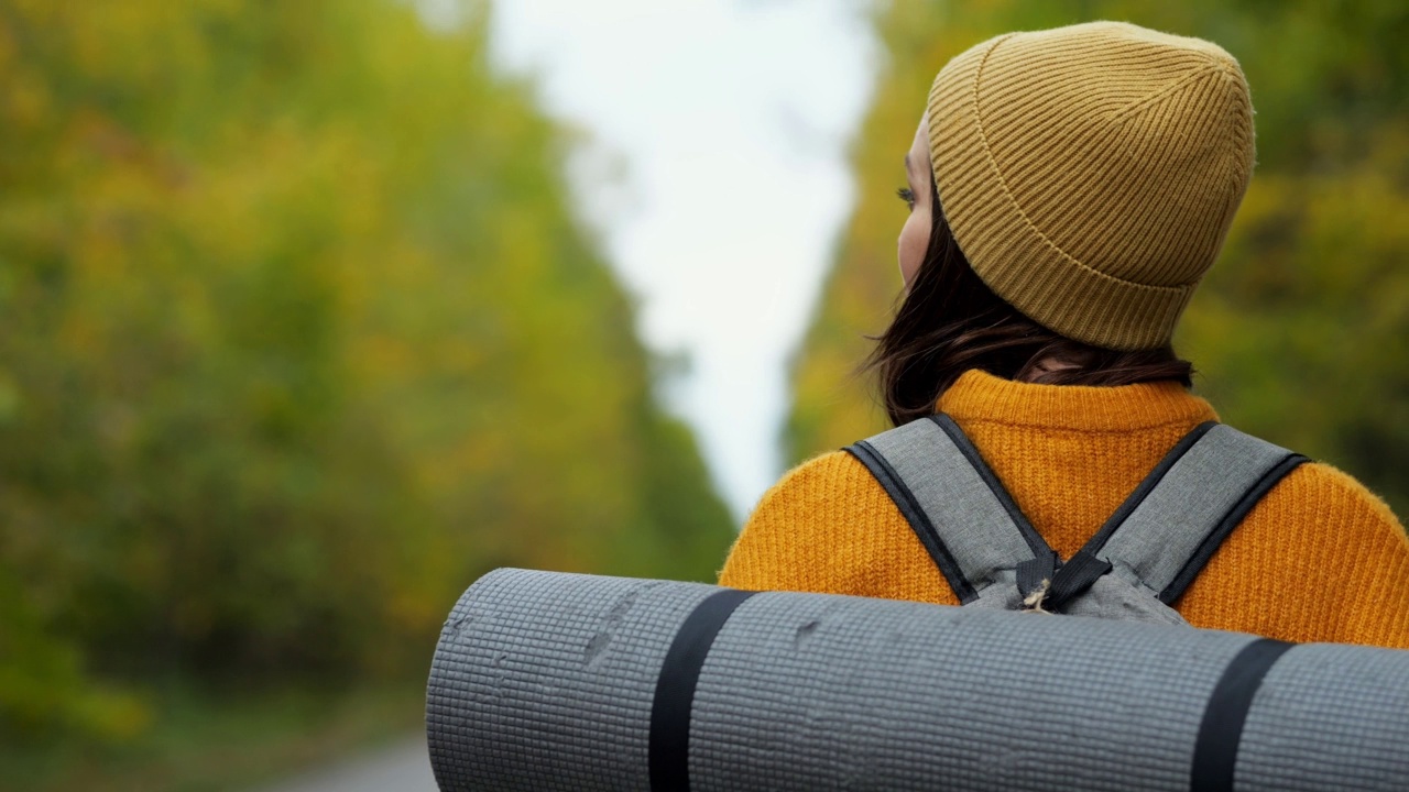 戴着温暖针织帽的女子徒步旅行者走在路上四处张望视频素材